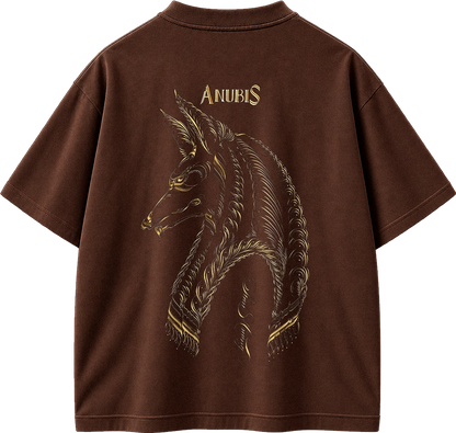 A brown short-sleeve t-shirt shown from the back, featuring a large gold-toned graphic of a horned animal head with the word 'ANUBIS' printed above it.