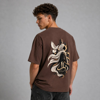A man viewed from behind wearing a brown t-shirt with a large graphic print on the back, featuring a stylized figure, flowing white and black elements, and Arabic calligraphy. He is also wearing dark gray jeans against a solid gray studio background.