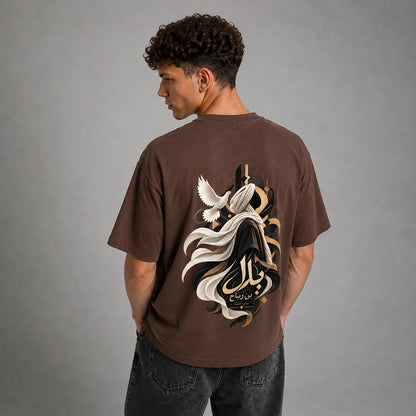 A man wearing a brown oversized t-shirt, viewed from the back. The shirt features a large graphic print of a white dove, a black and white flowing robe, and gold Arabic calligraphy.