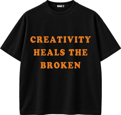 A black short-sleeve crewneck t-shirt with the phrase 'CREATIVITY HEALS THE BROKEN' printed in bold orange capital letters across the chest.
