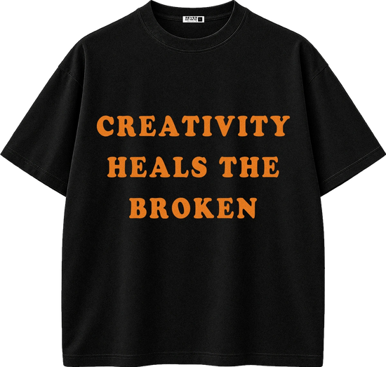 A black short-sleeve crewneck t-shirt with the phrase 'CREATIVITY HEALS THE BROKEN' printed in bold orange capital letters across the chest.