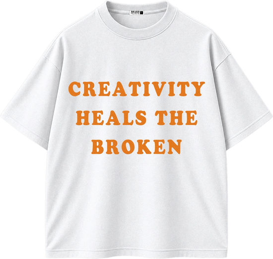 A white short-sleeve crewneck t-shirt with the phrase 'CREATIVITY HEALS THE BROKEN' printed in orange across the chest.