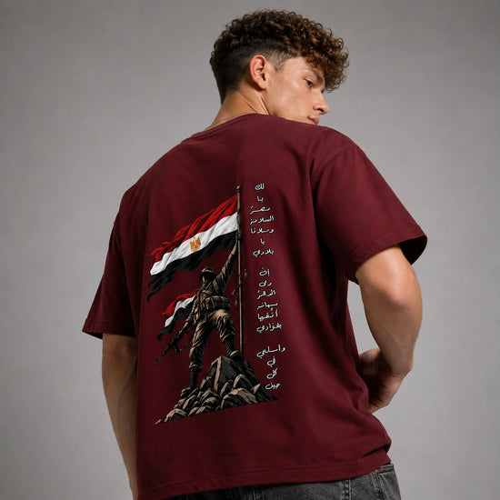 A man wearing a maroon t-shirt, viewed from the back. The shirt features a large graphic print of a soldier holding the Egyptian flag with Arabic text printed vertically on the back.