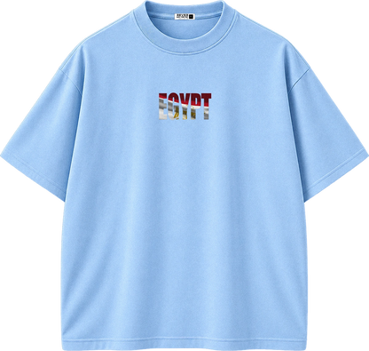 A light blue short-sleeve crewneck t-shirt with a graphic print on the chest spelling 'EGYPT' in a stylized font containing red, white, and blue elements. The shirt is displayed flat against a solid white background.