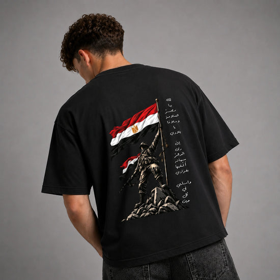 A man viewed from behind wearing a black t-shirt with a large graphic print on the back. The print features the Egyptian flag, a soldier statue, and vertical Arabic text.