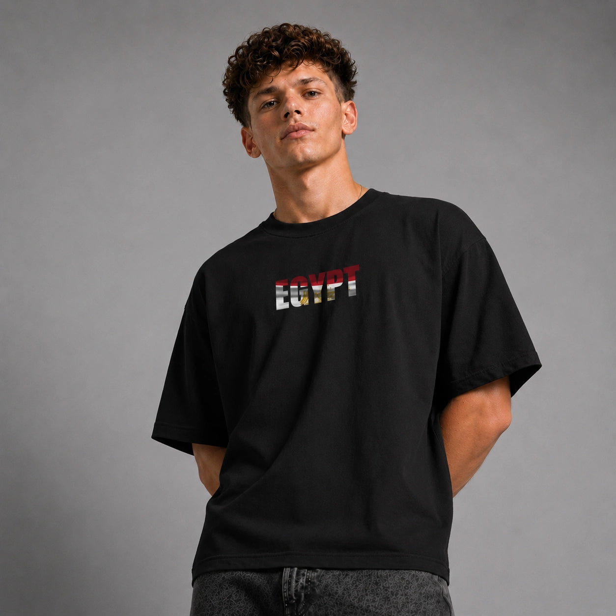 A young man wearing a black t-shirt with 'EGYPT' printed across the chest in the colors of the Egyptian flag, posed against a neutral gray studio background.