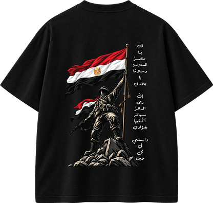 Black short-sleeve T-shirt shown from the back, featuring a large graphic print of a soldier holding an Egyptian flag on a rock, with additional Egyptian flag stripes and vertical Arabic text printed on the right side.