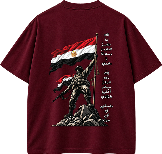 A dark maroon short-sleeve t-shirt shown from the back, featuring a graphic print of a soldier holding the Egyptian flag on a rocky outcrop, with vertical Arabic text printed on the right side.