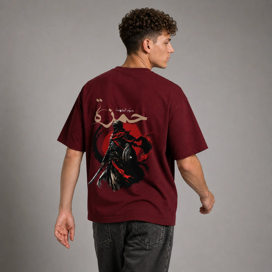 A man wearing a maroon short-sleeve t-shirt with a large graphic print on the back, shown from behind against a neutral gray studio background.