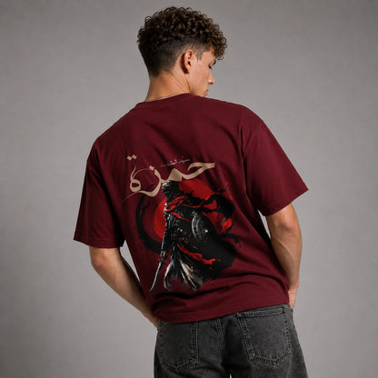 A man wearing a maroon t-shirt with a large graphic print on the back, shown from behind against a gray studio background.