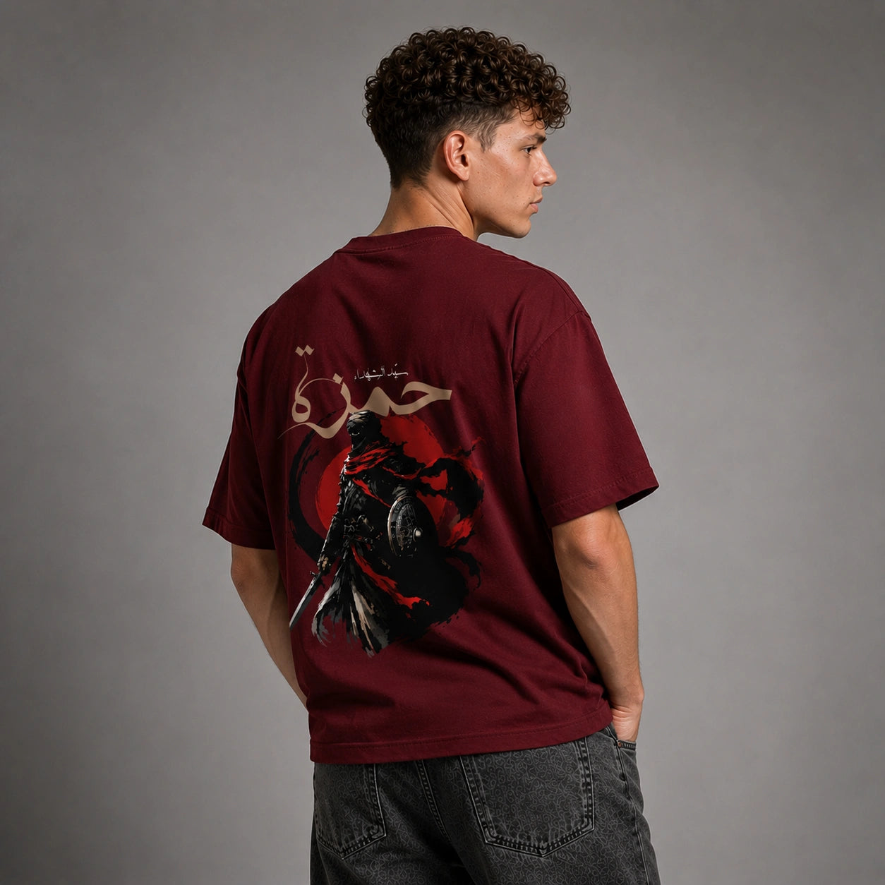 A man wearing a maroon t-shirt with a large graphic print on the back, shown from behind against a gray studio background.