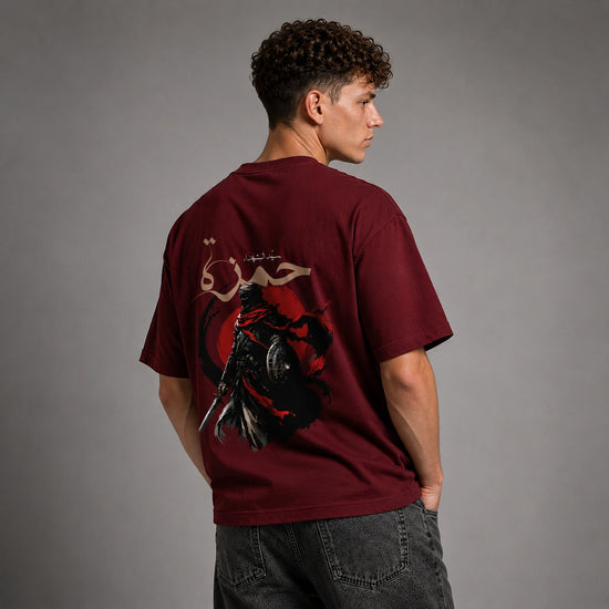 A man wearing a maroon t-shirt with a large graphic print on the back, shown from behind against a gray studio background.