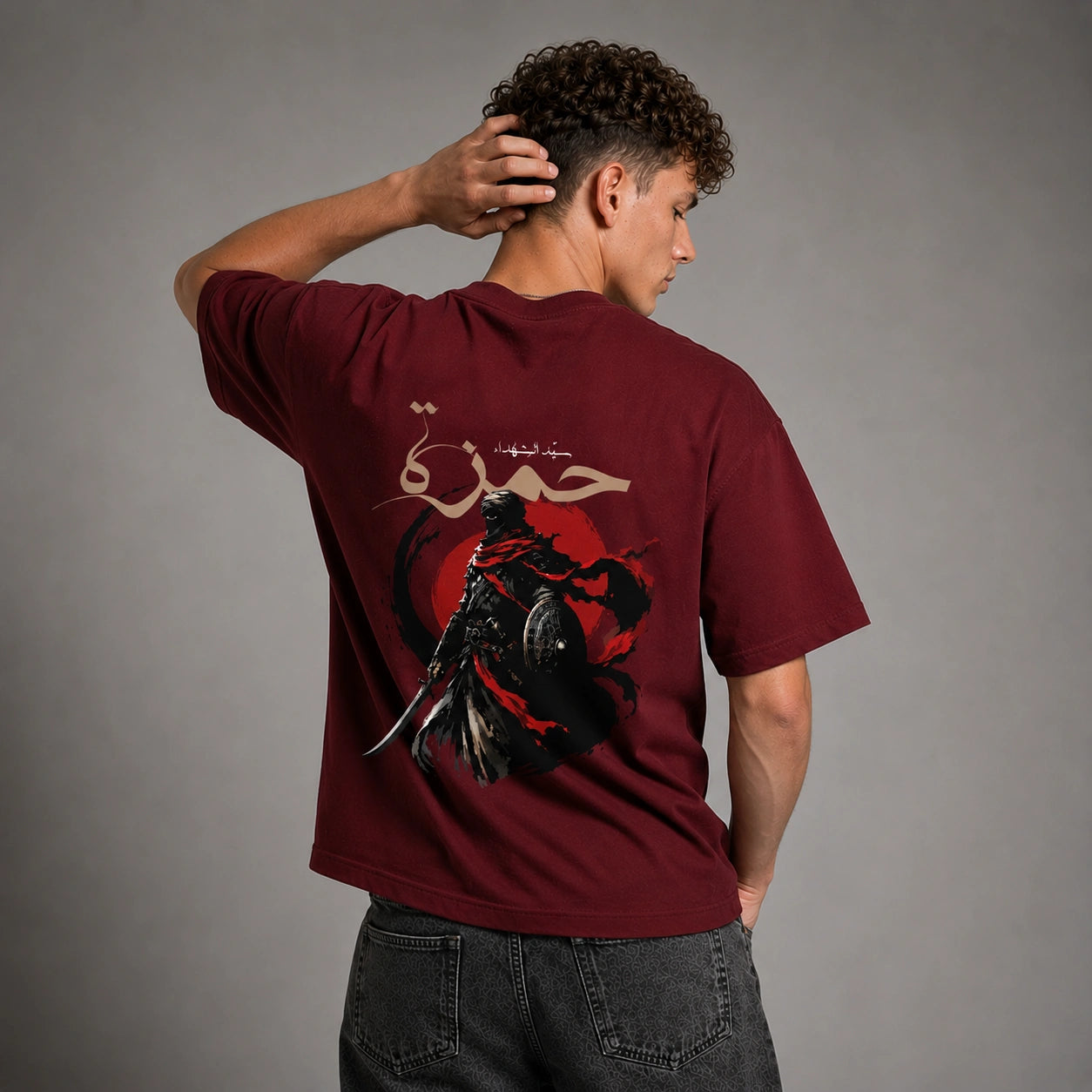 A man wearing a maroon t-shirt with a large graphic print on the back, shown from behind against a gray studio background.