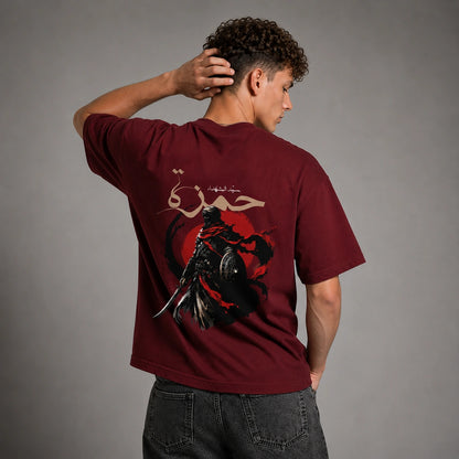 A man wearing a maroon t-shirt with a large graphic print on the back, shown from behind against a gray studio background.