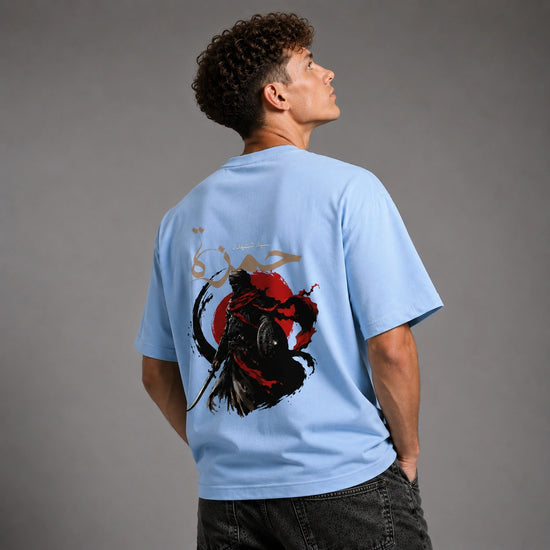 A man wearing a light blue t-shirt with a large graphic print on the back, shown from behind against a gray studio background.