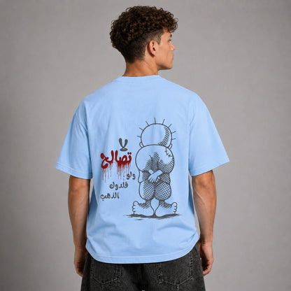 A man shown from the back wearing a light blue t-shirt with a large graphic print on the back. The graphic features a stylized cartoon character in black and gray, red Arabic text, and black Arabic calligraphy.