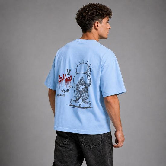 A man wearing a light blue t-shirt with a large graphic print on the back, shown from behind against a gray studio background.
