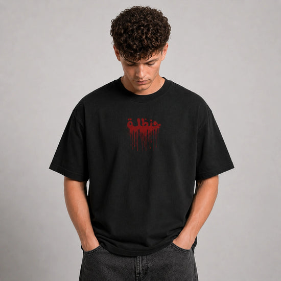 A man wearing a black crewneck t-shirt with a red dripping graphic on the chest, paired with dark gray jeans, standing against a neutral gray background.