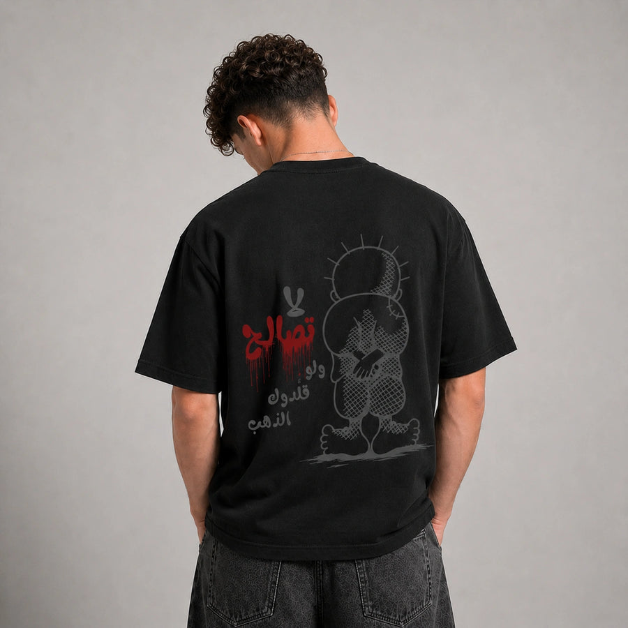 A man viewed from behind wearing a black graphic t-shirt with a red and gray design, paired with dark gray jeans, against a neutral gray studio background.