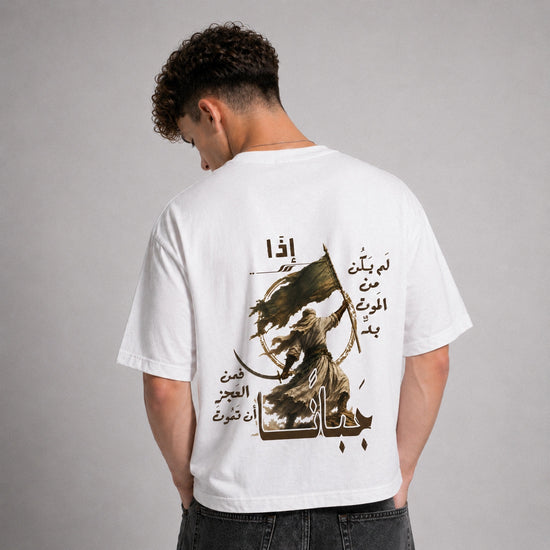 A man viewed from behind wearing a white short-sleeve t-shirt with a large brown graphic print featuring Arabic text and a stylized figure. He is also wearing dark gray jeans against a neutral gray studio background.