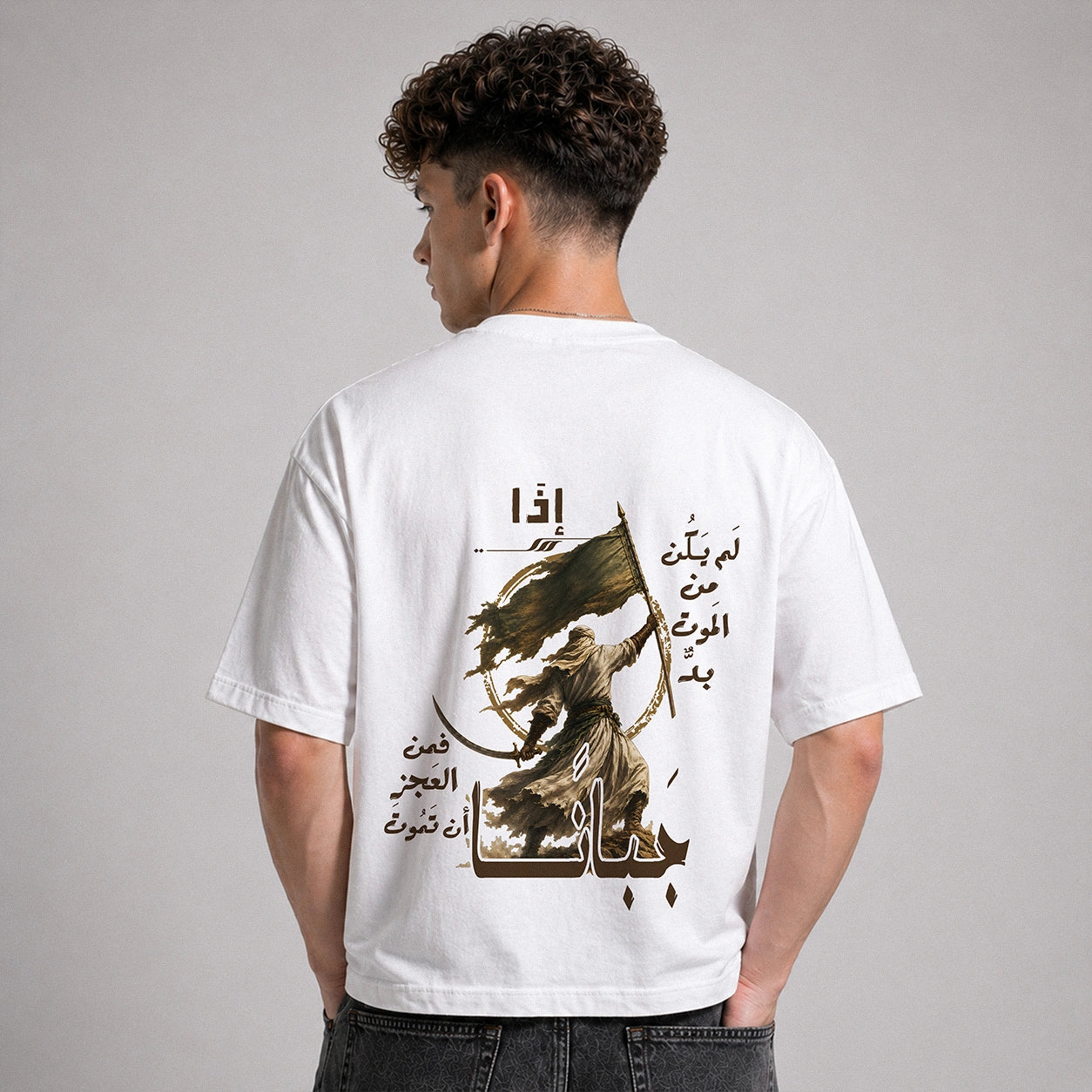 A man viewed from behind wearing a white t-shirt with a large graphic print on the back. The print features Arabic calligraphy and an illustration of a figure holding a sword and flag.
