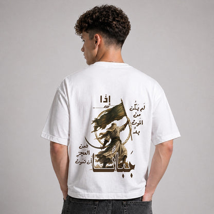 A man viewed from behind wearing a white t-shirt with a large graphic print on the back. The print features Arabic calligraphy and an illustration of a figure holding a sword and flag.