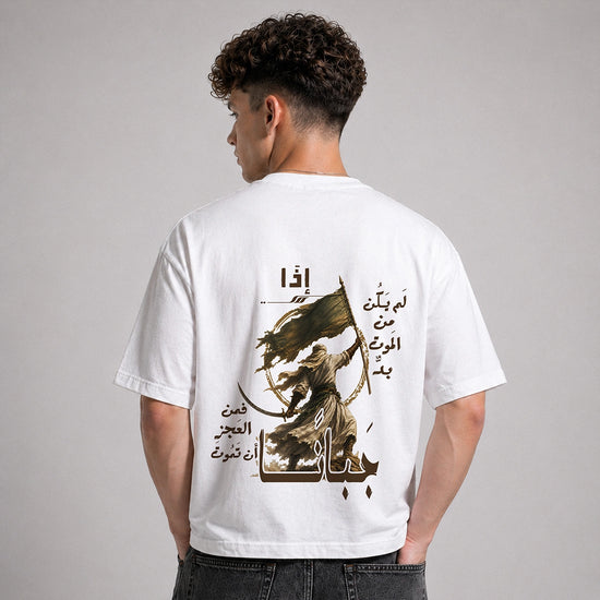 A man viewed from behind wearing a white t-shirt with a large graphic print on the back. The print features Arabic calligraphy and an illustration of a figure holding a sword and flag.