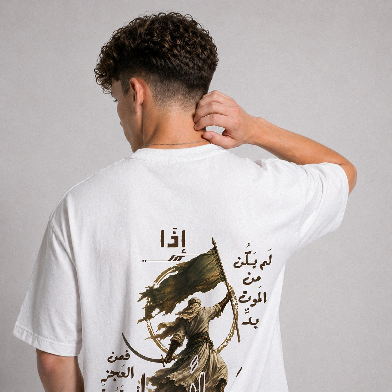 A man viewed from behind wearing a white t-shirt with a large graphic print on the back. The print features Arabic calligraphy and an illustration of a figure holding a flag.