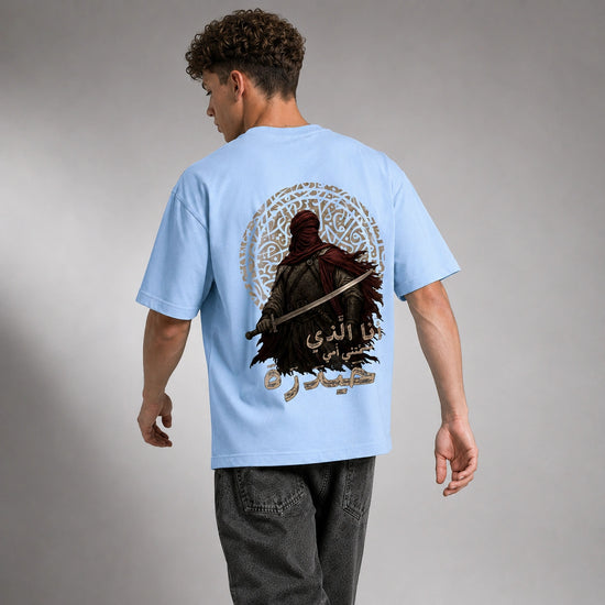 A man wearing a light blue t-shirt with a large graphic print on the back, shown from behind against a gray studio background.