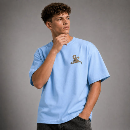 A man wearing a light blue crewneck t-shirt with a small brown embroidered rabbit logo on the left chest, posed against a neutral gray studio background.