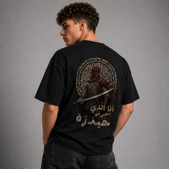 A man wearing a black t-shirt with a large graphic print on the back, shown from behind against a gray studio background.