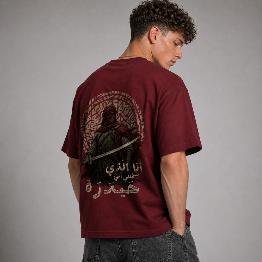A man wearing a maroon t-shirt with a large graphic print on the back, photographed from behind against a neutral gray studio background.