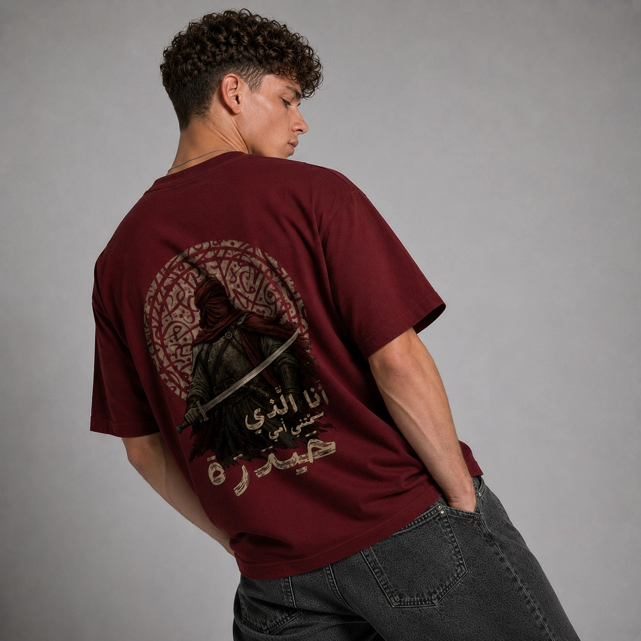 A man wearing a maroon t-shirt with a large graphic print on the back, photographed from behind against a neutral gray background.