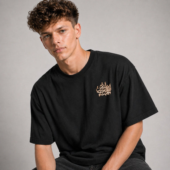 Man wearing a black t-shirt with Arabic text on a gray background