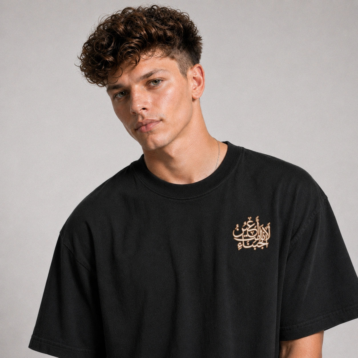 Man wearing a black t-shirt with Arabic text on a gray background