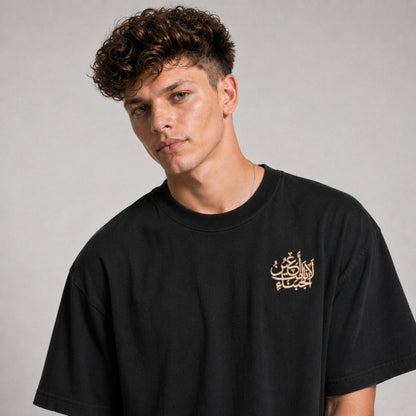 Man wearing a black t-shirt with Arabic text on a gray background