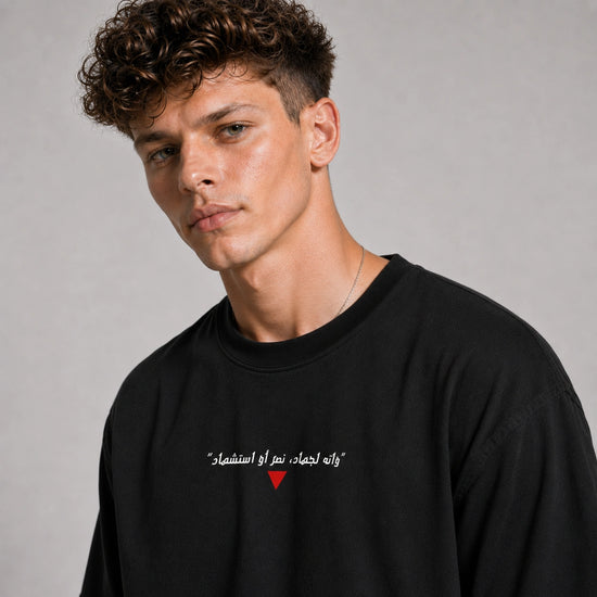 Man wearing a black sweatshirt with Arabic text and a red heart symbol on a gray background