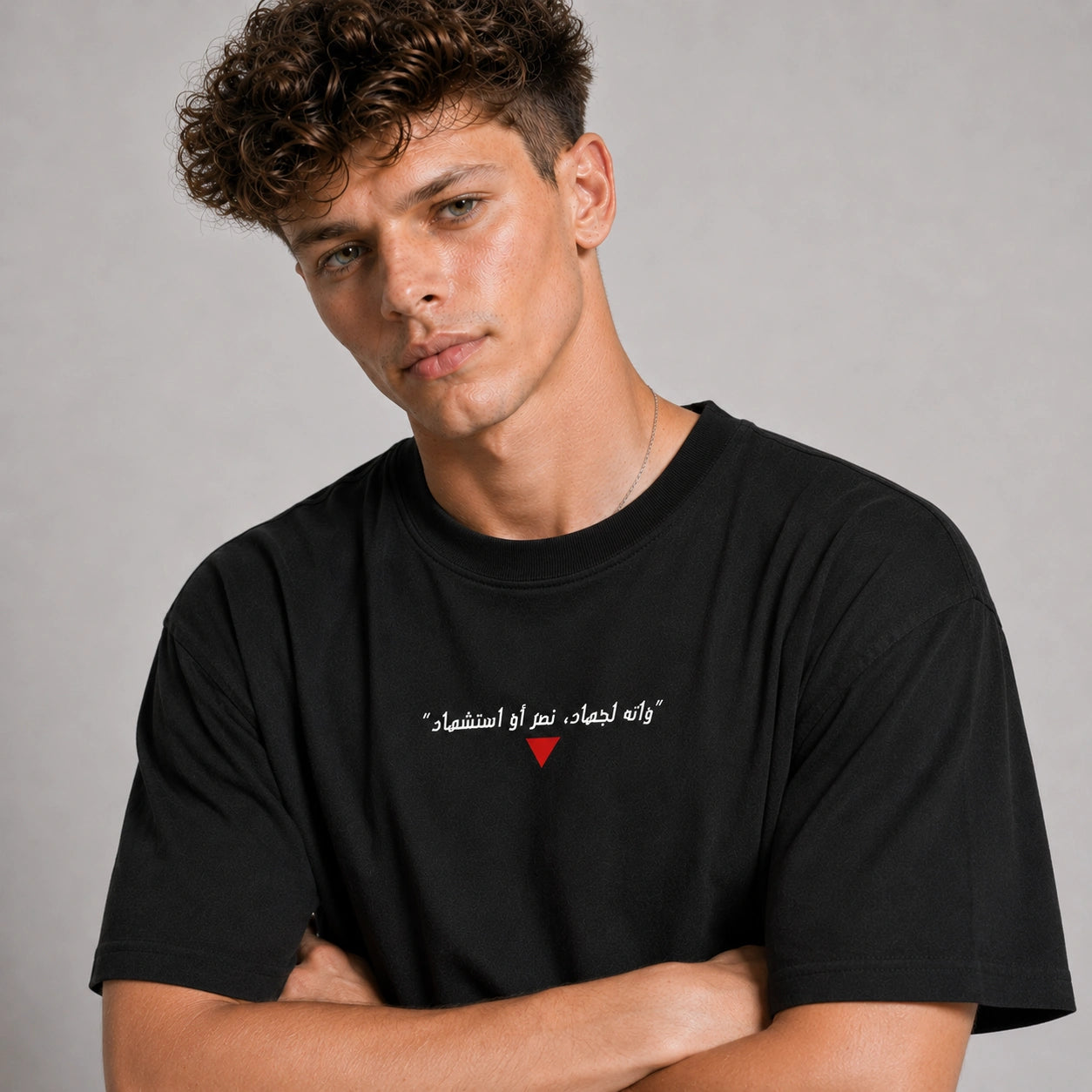 Man wearing a black t-shirt with Arabic text and a red heart symbol on a gray background