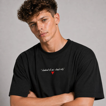Man wearing a black t-shirt with Arabic text and a red heart symbol on a gray background