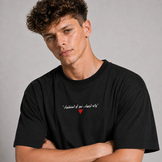 Man wearing a black t-shirt with Arabic text and a red heart symbol on a gray background