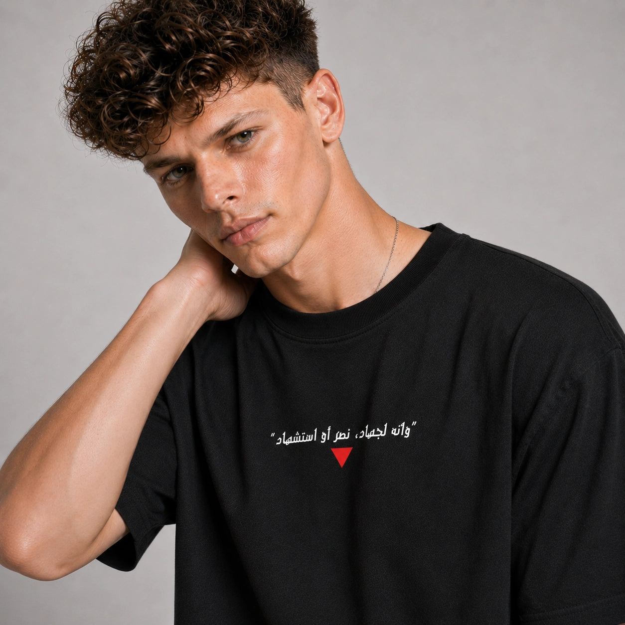 Man wearing a black t-shirt with Arabic text and a red heart symbol on a gray background