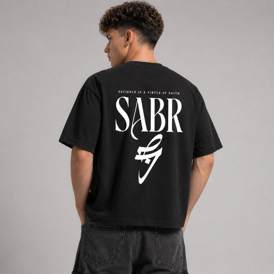 Person wearing a black t-shirt with 'SABR' logo and text on the back, standing against a gray background