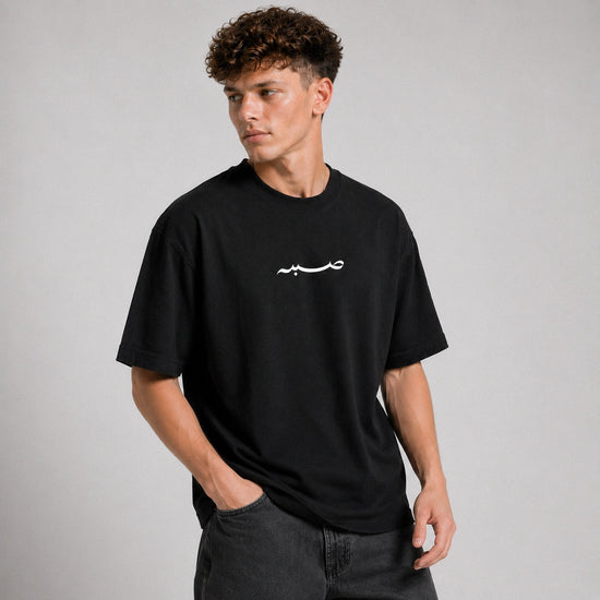 Man wearing a black t-shirt with a white logo on a gray background