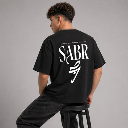 Person wearing a black t-shirt with 'SABR' logo and text on the back, sitting on a stool against a gray background.