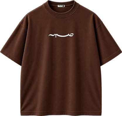 A brown short-sleeve crewneck t-shirt with a white Arabic calligraphy graphic printed on the chest, displayed on a clean white background.