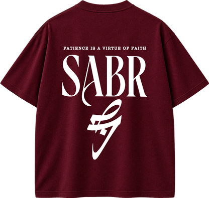 A maroon short-sleeve t-shirt shown from the back, featuring a large white graphic print with the text 'PATIENCE IS A VIRTUE OF FAITH' and 'SABR' in a stylized font.