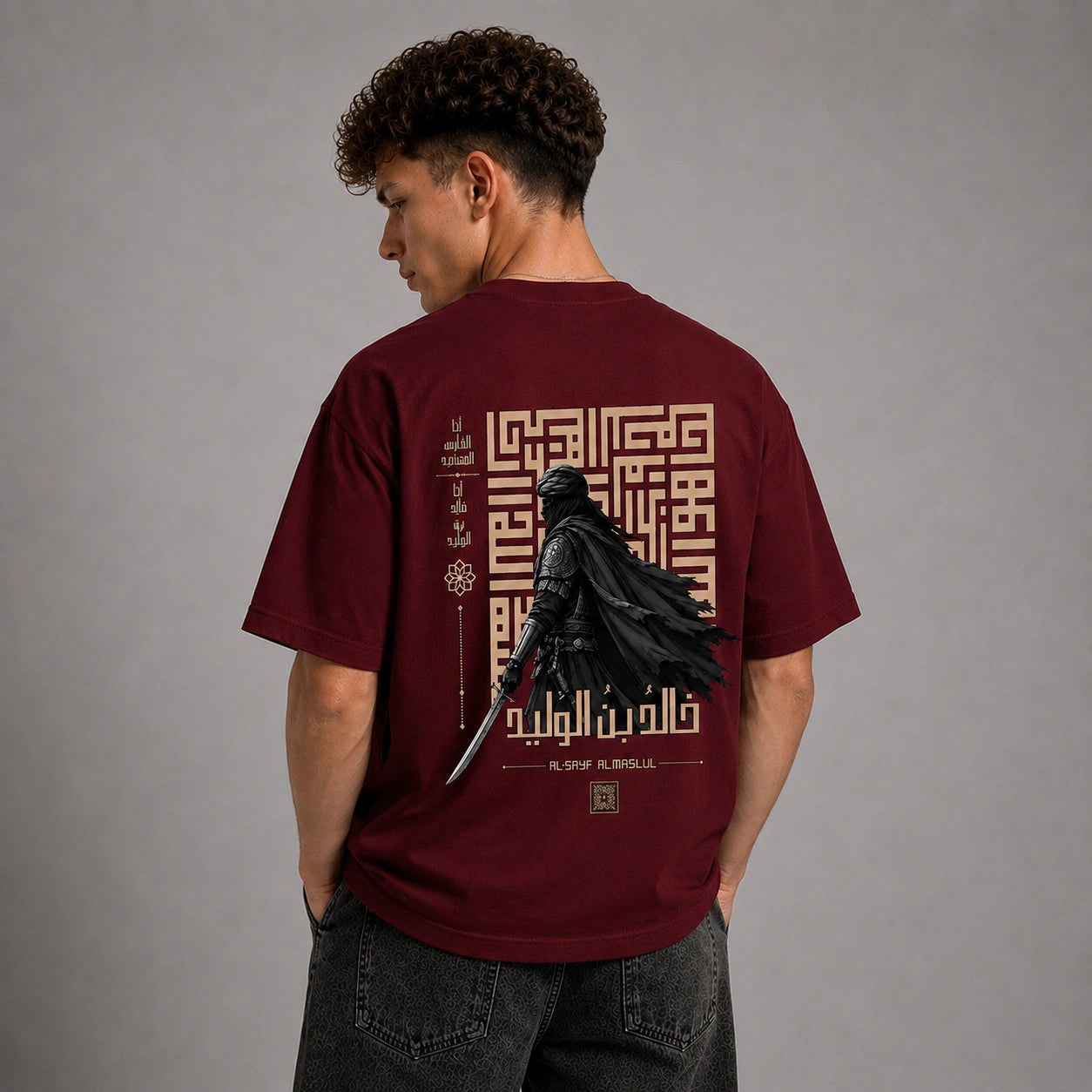 A man wearing a maroon short-sleeve t-shirt, viewed from the back. The shirt features a large graphic print of a black knight in chainmail holding a sword, surrounded by gold Arabic calligraphy and geometric patterns.