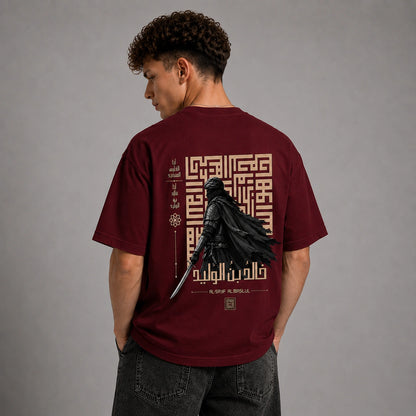 A man wearing a maroon short-sleeve t-shirt, viewed from the back. The shirt features a large graphic print of a black knight in chainmail holding a sword, surrounded by gold Arabic calligraphy and geometric patterns.