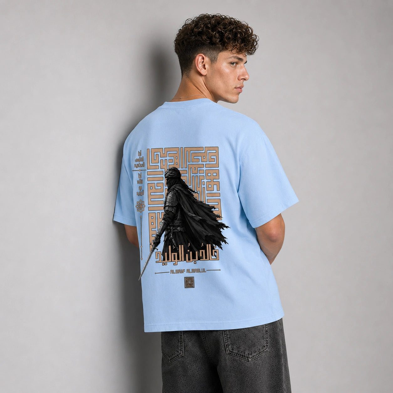 A man wearing a light blue t-shirt with a large Darth Vader graphic on the back, shown from behind against a neutral gray background.