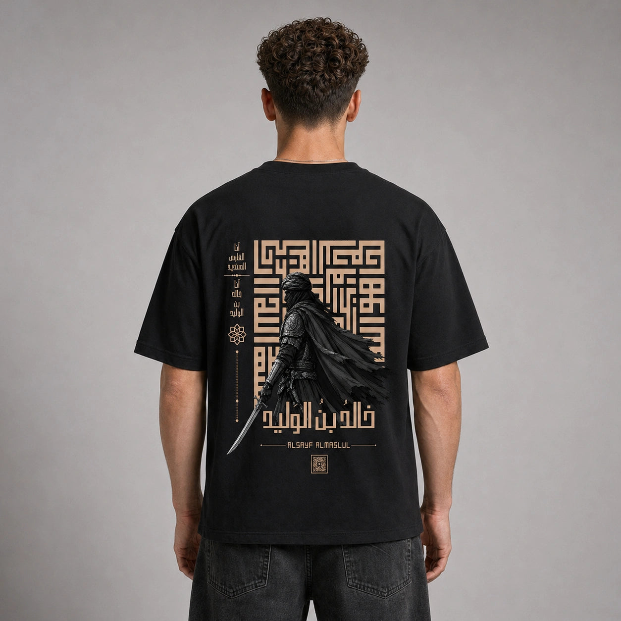 A man viewed from behind wearing a black t-shirt with a large graphic print on the back. The graphic features a dark knight in a flowing cape holding a sword, set against a beige geometric maze and Arabic calligraphy.